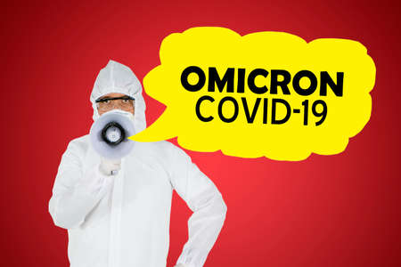 Male doctor using a megaphone to announcing Omicron covid-19 variant while standing in the studio with red backgroundの写真素材