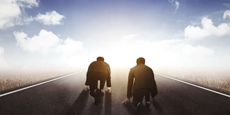 Rear view of two businessmen ready to running while kneeling on the road toward sunlightの写真素材