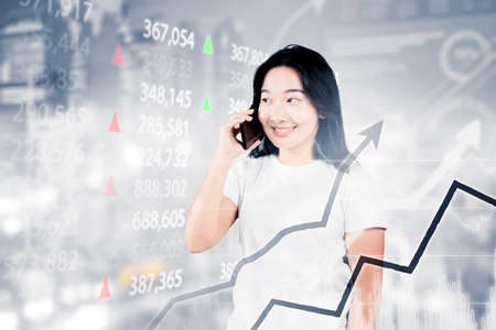 Picture of young woman talking on a mobile phone while standing with increasing stock market graph...