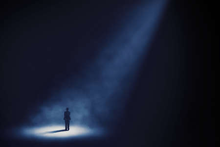 Rear view of businessman looks confident while standing under light in the dark roomの写真素材