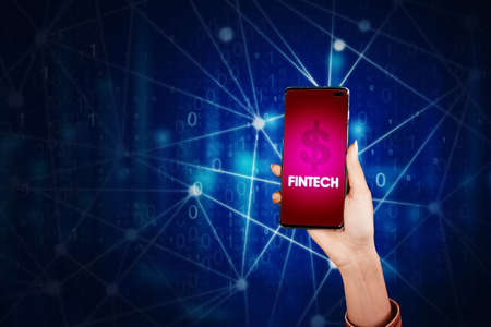 Young woman showing fintech app on the mobile phone while standing in the cyberspace with virtual screen backgroundの写真素材