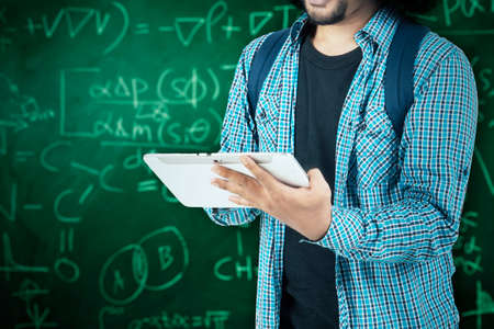 Close up of male college student hands using a digital tablet while standing in the classroom with...