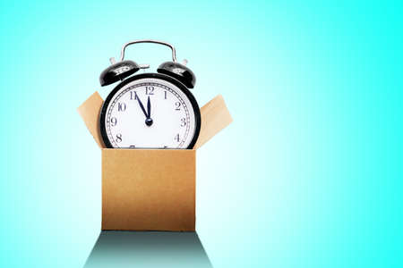 Image of alarm clock get out from the cardboard box in the studio with tosca background