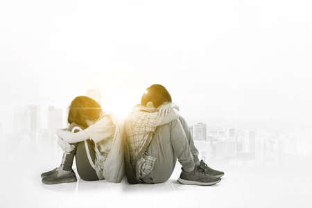 Double exposure of two little students looks sad while sitting together with cityscape background
