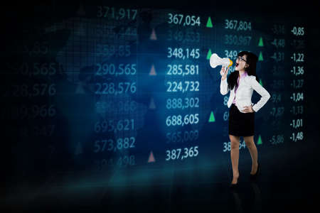 Businesswoman using a megaphone while standing with stock trade background