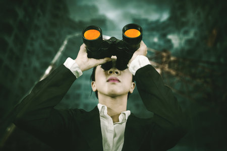 Low angle view of female manager using binoculars while standing with cloudy sky backgroundの写真素材