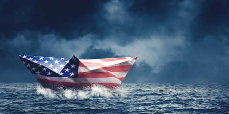 Paper boat with America flag floating on the sea with cloudy sky backgroundの写真素材