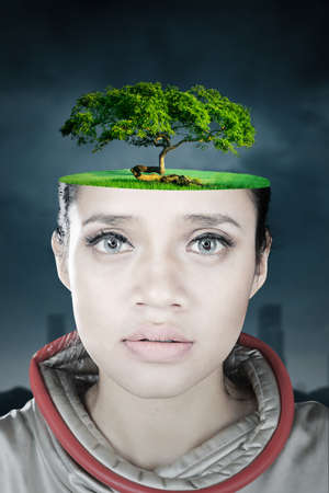 Close up of green tree on futuristic woman head with cloudy sky. Shot in the polluted cityの写真素材