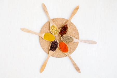 Top down view of wooden spoons and plate with various spices on the white table. Isolated on white...