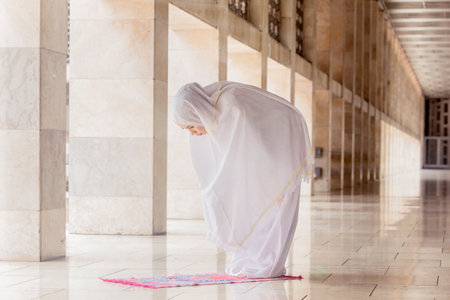Young woman wearing a prayer clothes while doing Salat with ruku gesture in the mosqueの写真素材