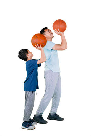 Happy father teaching his son to shooting a basketball while exercising together in the studio....