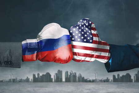 Two hands wearing boxing gloves with Russia and America flag while hitting each other with cloudy sky backgroundの写真素材