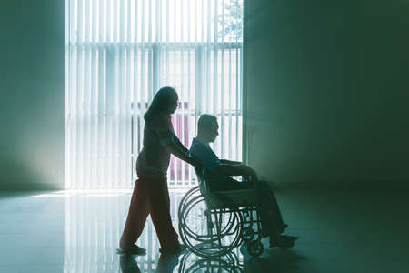 Silhouette of old woman pushing her husband on a wheelchair after recovering from stroke disease