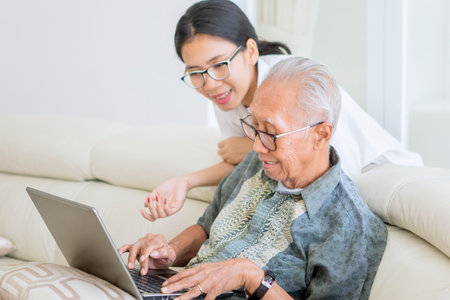 Young woman guiding her father how to use a laptop while sitting on the sofa. Shot at home