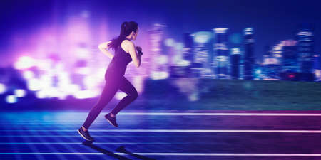 Rear view of young woman running fast on the track with blurred glowing city backgroundの写真素材