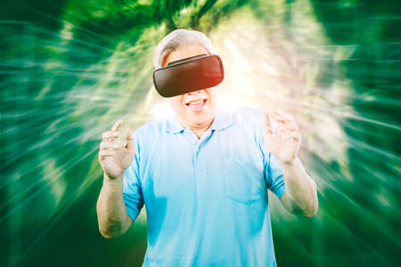 Happy old man wearing VR goggles while playing games in the metaverse with virtual screen backgroundの写真素材