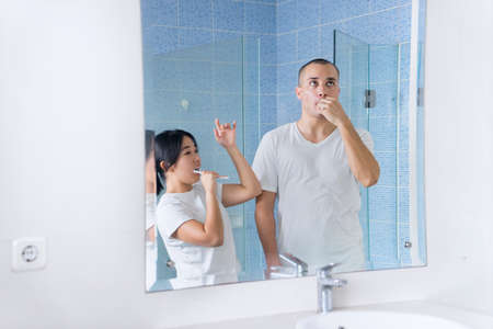 Cheerful young couple brushing their teeth while dancing together in front of a mirror in bathroom....