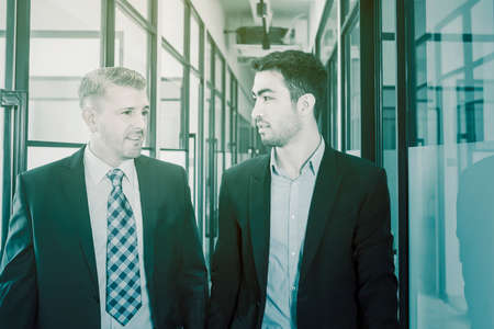 Portrait of two business people chatting together while walking in the office corridor