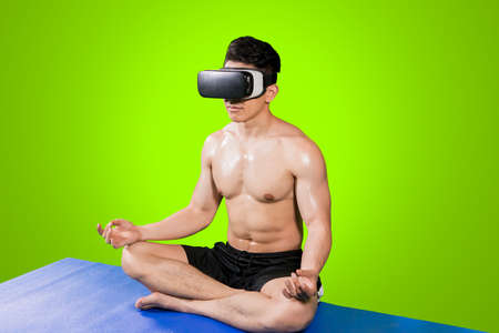 Image of muscle man wearing VR glasses while doing meditation in the studio with green screen...