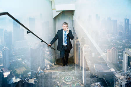 Double exposure of male manager make a phone call while climbing stairs with cityscape backgroundの写真素材