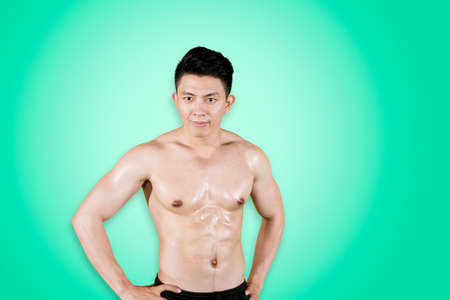 Sporty young man smiling at the camera while standing in the studio with green screen background