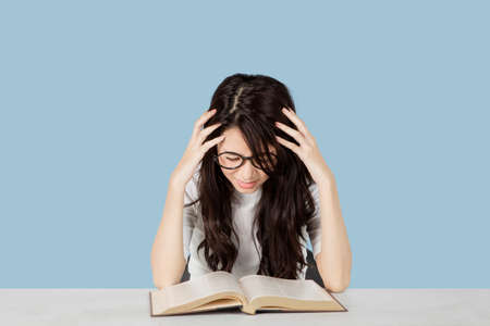 Female student looks depressed while studying with book in the studio with gray backgroundの写真素材