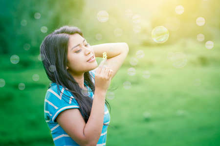 Beautiful woman blowing soap bubble while standing at the park with sunlight backgroundの写真素材