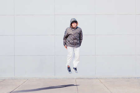 Hoodie male dancer jumping while performing break dance at the outdoors