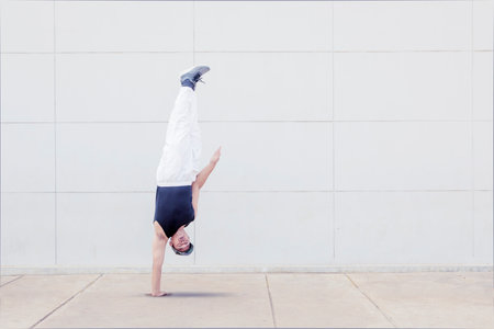 Young male hip hop dancer doing handstand while performing in the studio with white wall background
