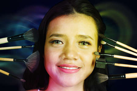 Close up of female model face doing makeup with variety cosmetic brushes while smiling at the camera