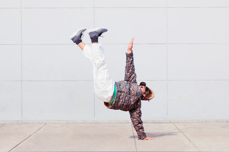 Young man wearing sweater while doing hip hop dance with handstand pose