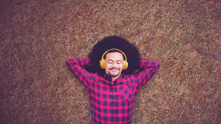 Top down view of young man enjoying music with headset while lying on the grass at parkの写真素材