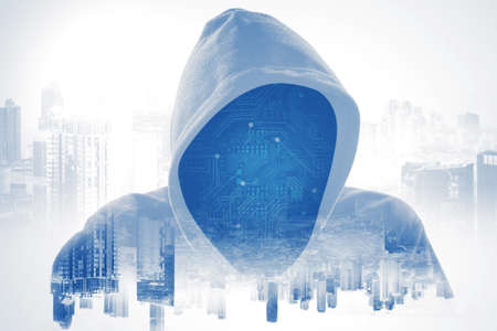 Double exposure of hooded hacker with digital circuit board face in modern cityscape background