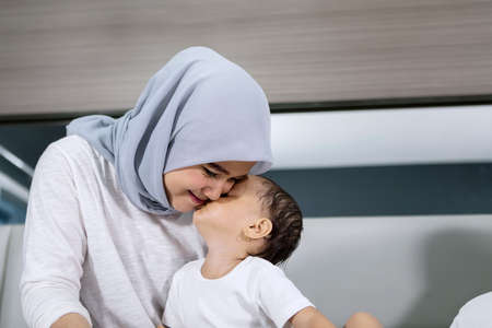 Muslim woman kissed by her baby girl while sitting on the bed. Shot at homeの写真素材