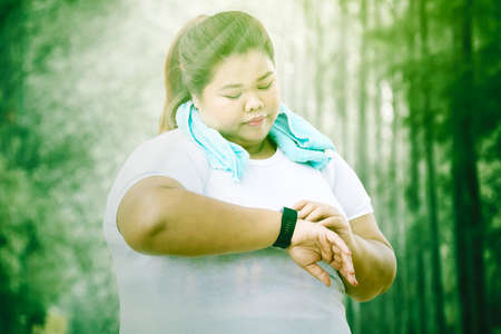 Fat woman setting smart watch before exercise at the park with sunlight background