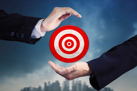 Close up of businessman hands showing a red dartboard with cityscape background