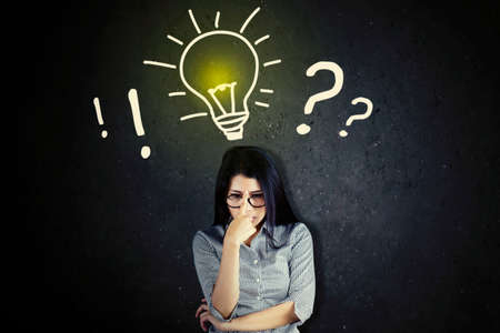 Businesswoman concentrating while standing with a bright light bulb and question mark