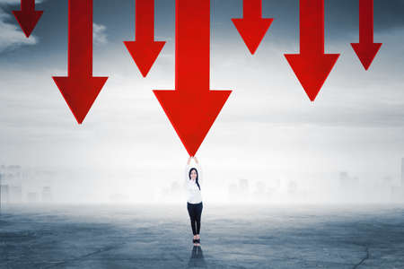 Happy businesswoman try to hold falling arrows while standing with cloudy sky backgroundの写真素材