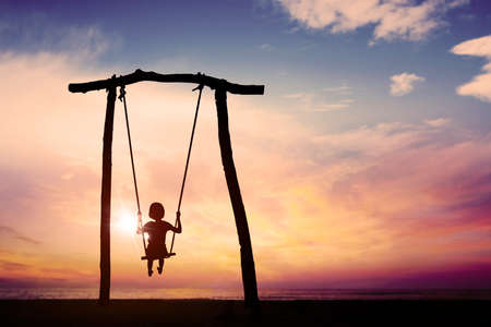 Silhouette of little girl playing with swings on the beach while enjoying sunset viewの写真素材