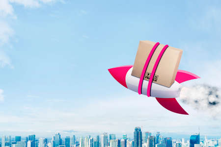 Red rocket carrying a package box while flying above the modern city with blue sky backgroundの写真素材