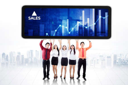 Group of business people lifting a cellphone with growth sales chart while standing with modern city backgroundの写真素材