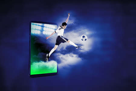 Soccer player jumping out from cellphone screen while kicking a ball in the cyberspaceの写真素材
