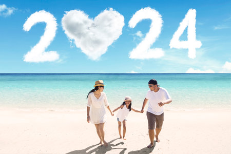 Little girl holding hands her parents while walking on the beach with clouds shaped 2024 new year numbers and heart in the blue skyの写真素材