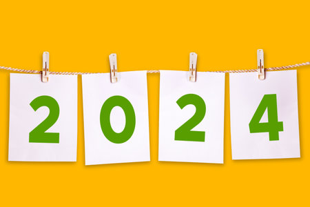 Close up of white papers with 2024 new year numbers hanging on the rope isolated over orange backgroundの写真素材