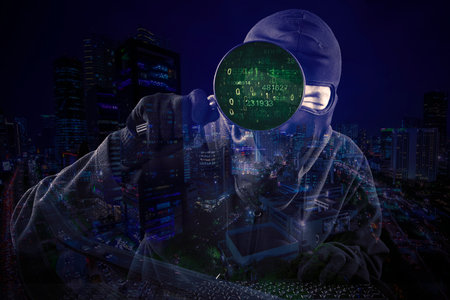 Internet Theft - a hooded man looking at computer screen using magnifying glass with cityscape night...