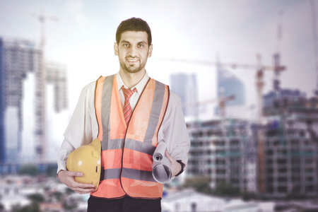 Civil Engineer Hispanic holding a blueprint and helmet smiling with Construction backgroundの写真素材
