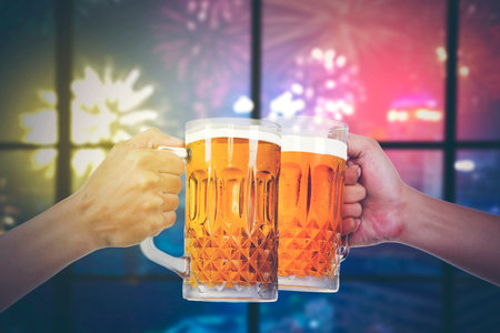 Closeup of hands toasting with bottles of beer at the party club with fireworsk display outsideの写真素材