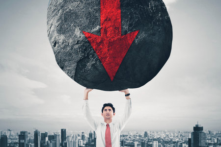 Businessman lifting a huge rock with a red downward arrowの写真素材