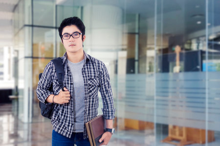 Photo of serious young male student standing in front of glass doorの写真素材