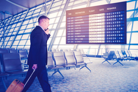 Caucasian businessman using smartphone while walking with suitcase at airport terminalの写真素材